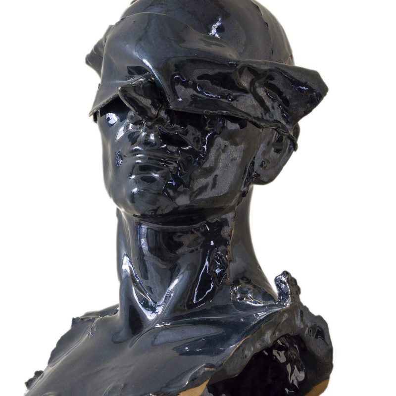 Busto in ceramica nero raffigurante il volto silenzioso di un uomo calvo a cui vengono velati gli occhi